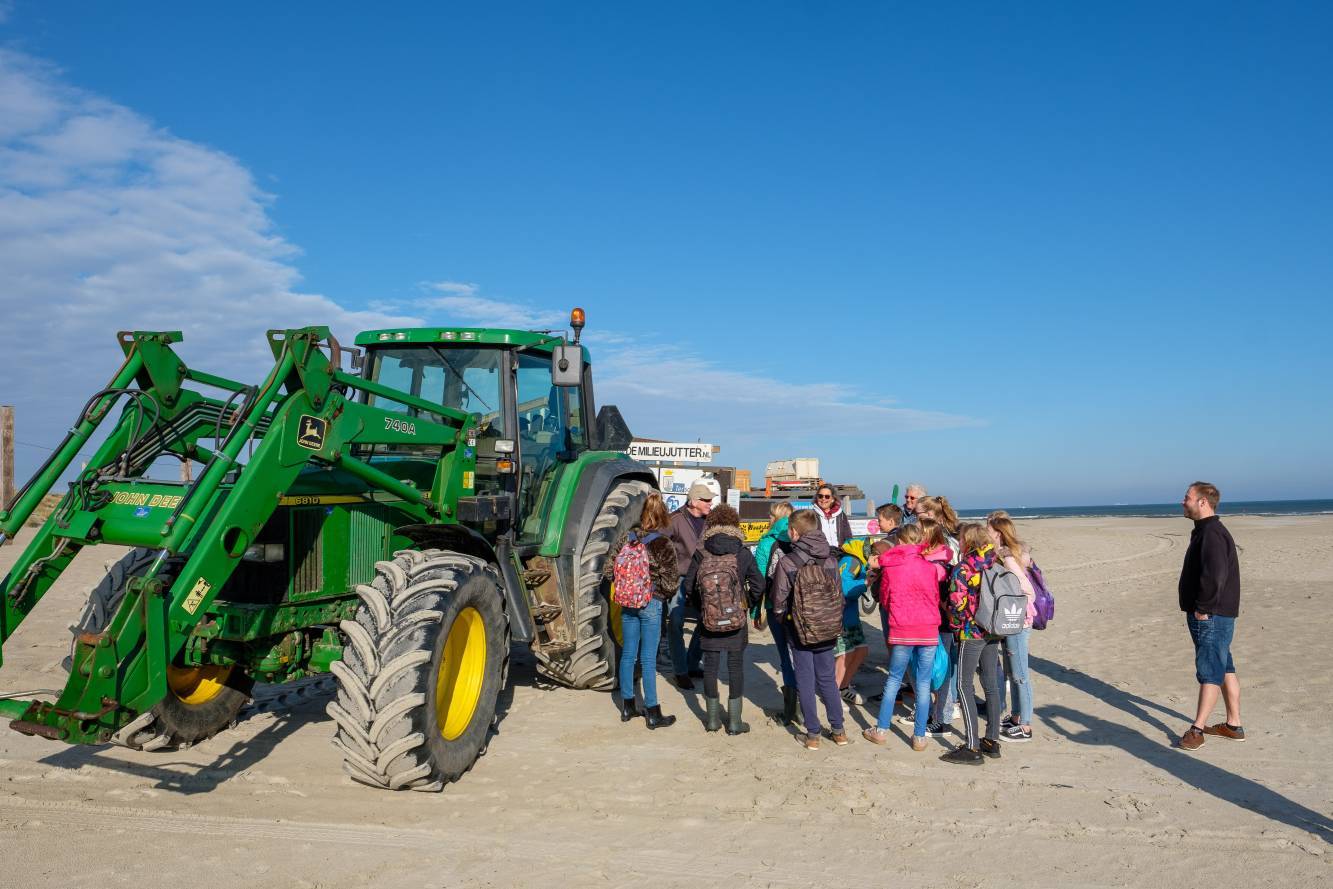 Groep schoolkinderen bij tractor Milieujutter op het strand